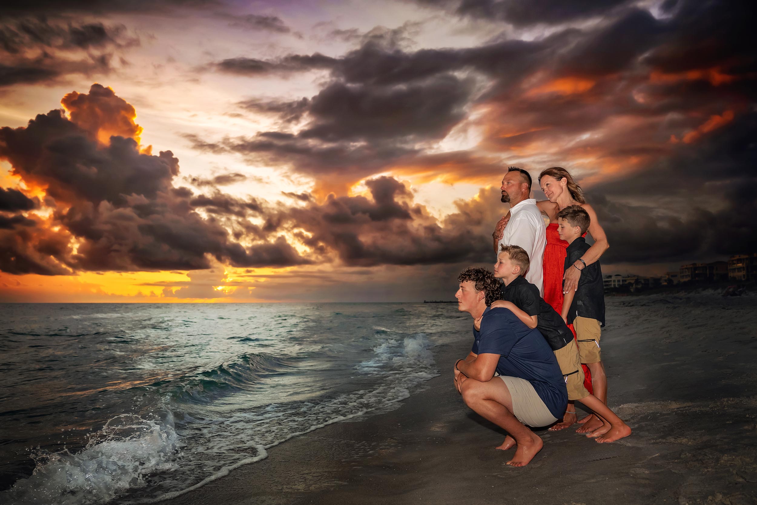 family huddled together on Longboat Key beach at sunset looking over the water with dramatic sky