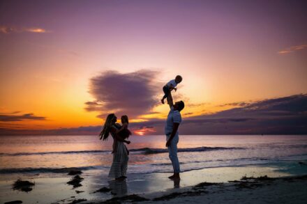silhouette of mom and dad holding children on beach with sunset background