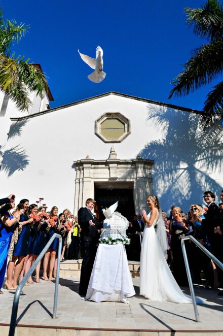 bride and groom excitedly releasing flying doves from basket in front of church