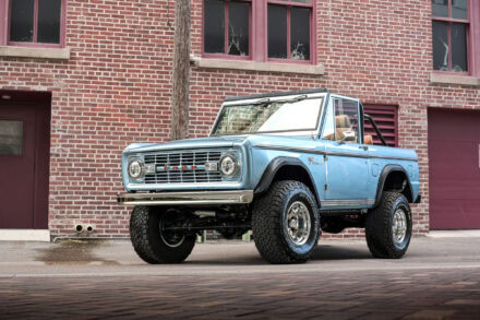 driver front angle view of vintage 1977 blue ford bronco parked in front of red brick building