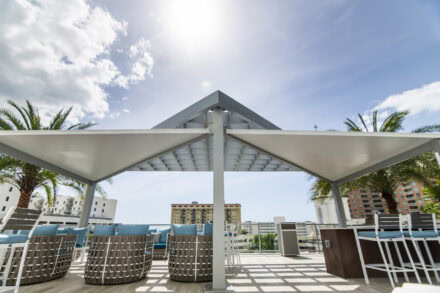 custom modern aluminum pergola with white shade installed on pool deck with outdoor chairs underneath