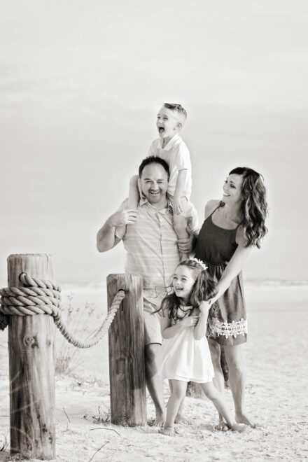 black and white image of parents and 2 children laughing together on sandy beach