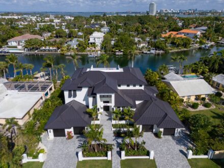 aerial drone image of large canal front home with dark bronze metal roof