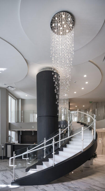 curved glass railing staircase in condo lobby with long crystal chandelier