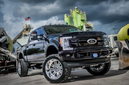 ford f250 with fox suspension, bds, and specialty forged wheels at concrete facility with american flag flying in background