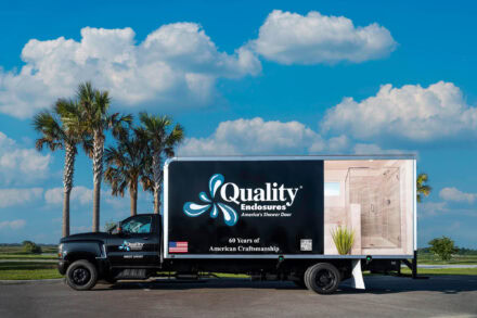 black commercial box delivery truck with quality enclosure logo against blue sky and white clouds and palm tree backdrop