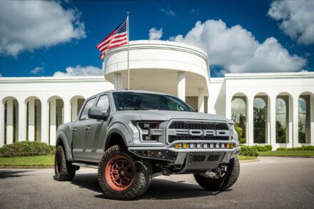 matte grey ford raptor with red wheels in front of white building with columns and american flag