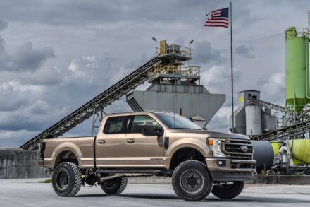 light brown custom painted ford f250 lifted truck with american flag and cement factory backdrop