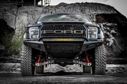 front end of a lifted black ford raptor in front of large dirt pile