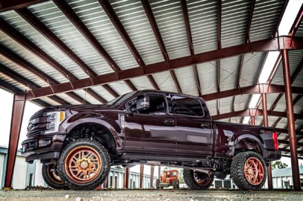 Lifted Ford f250 with rose gold specialty forged wheels parked under a covered area