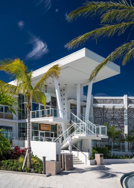 white modern architectural building with glass railing, palm trees, and blue skies