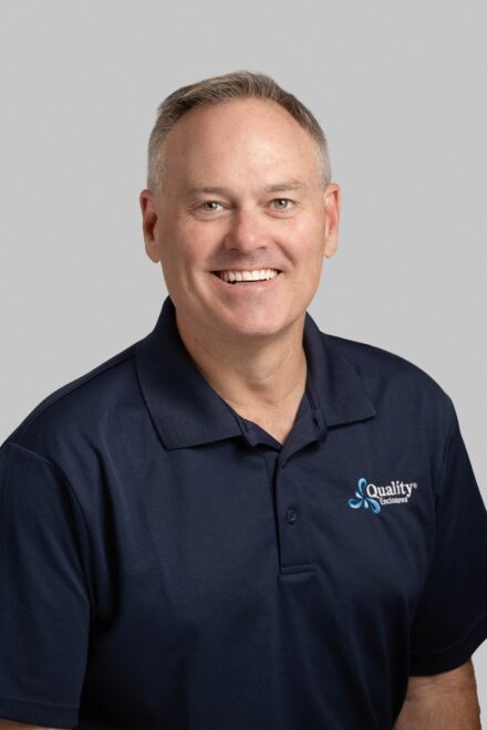 Professional headshot of man with brown eyes and dark blue polo with quality enclosures logo