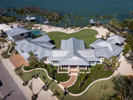large residence on palm tree lined bay with green turf and metal roof
