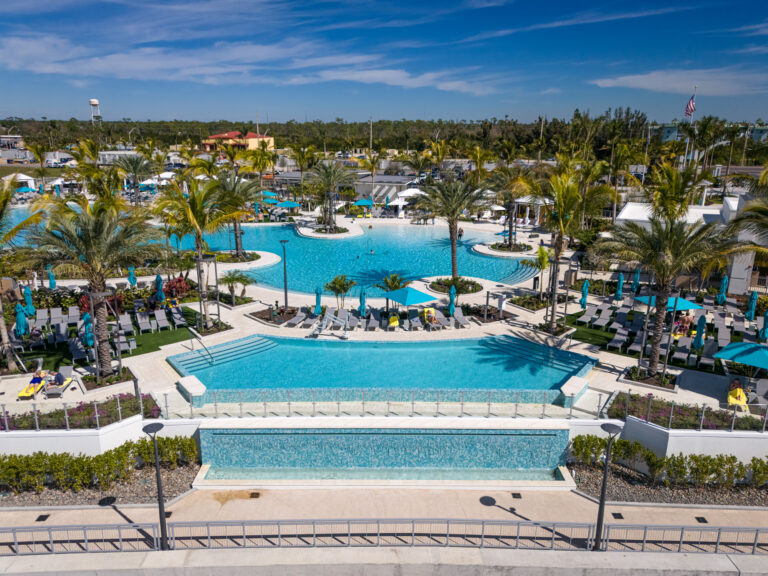 aerial view of a large hotel pool with sunbathers, tropical landscaping, glass railing, and cable railing