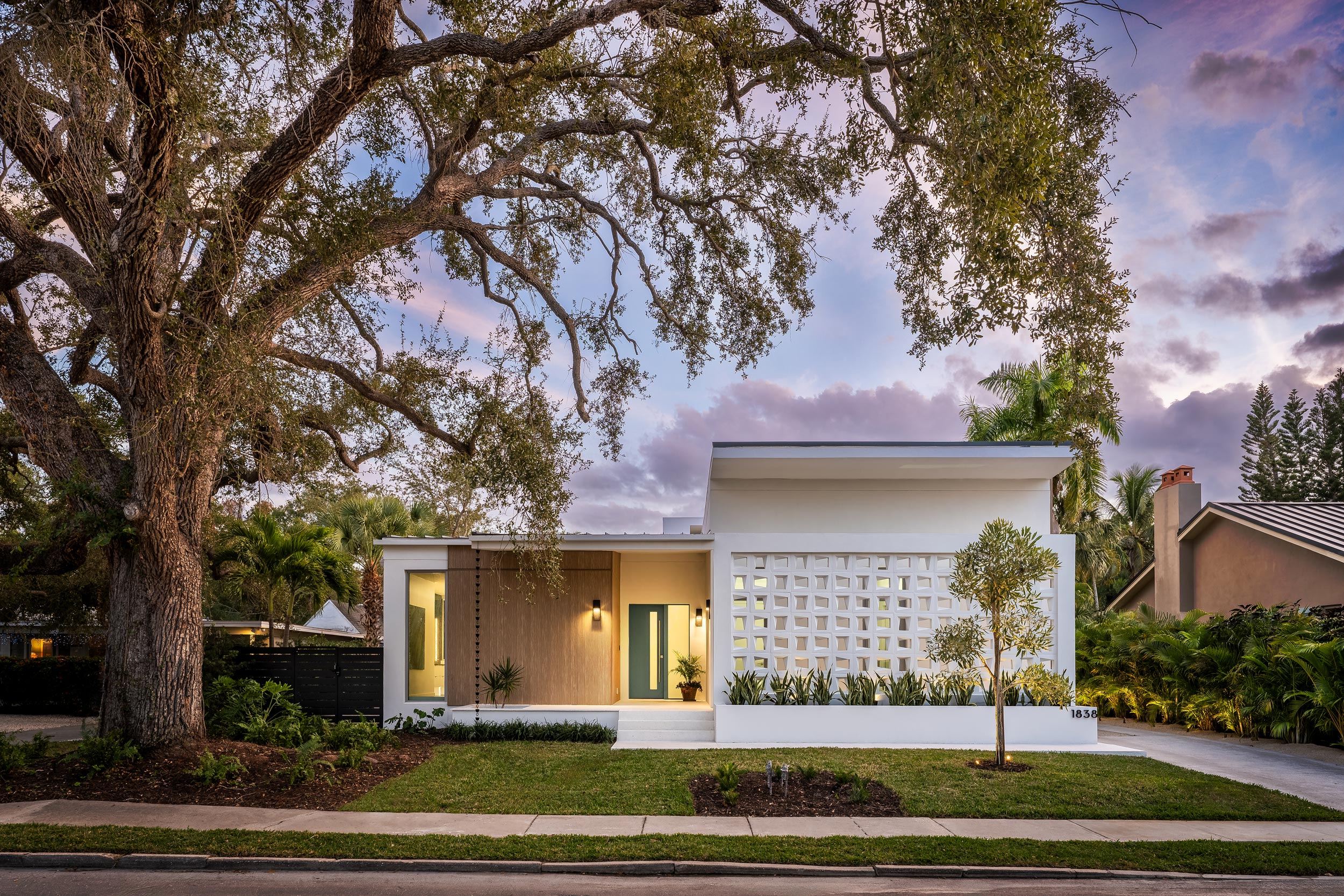 An architectural photograph of a modern residence in the Avondale Park Community Sarasota, Fl with custom breeze block and a large oak tree against a dusk sky