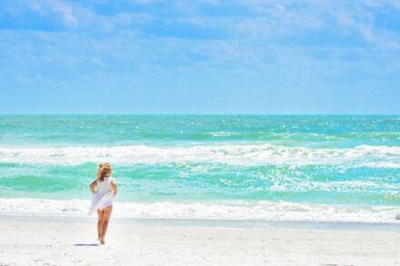 small little girl running towards beach, holding up white dress