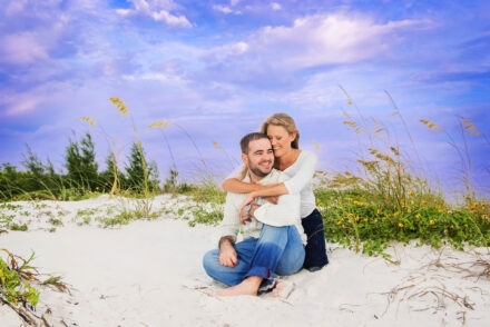 man sitting on Siesta Key with woman's arms wrapped around him from behind smiling