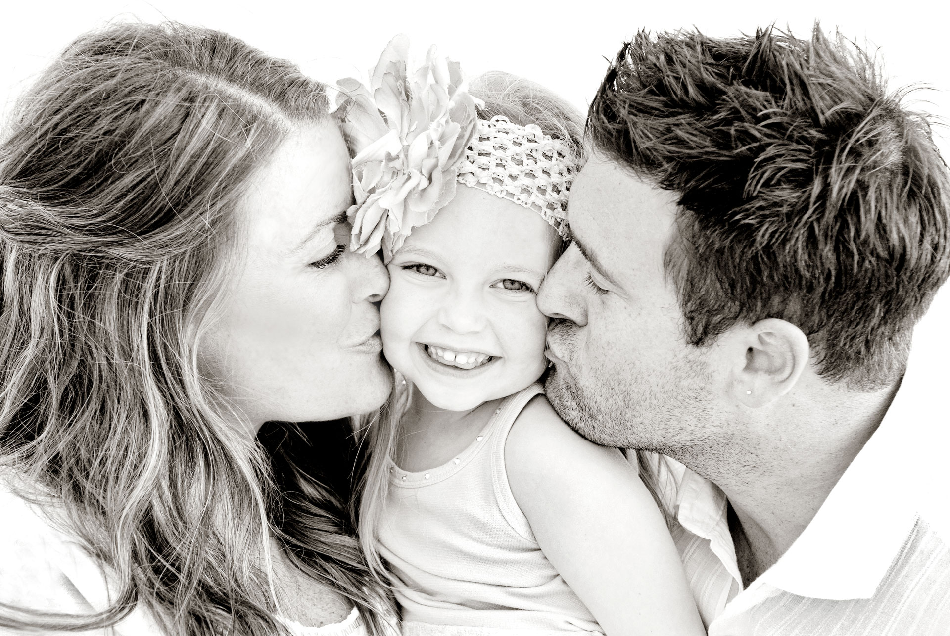 mother and father kissing their smiling daughter with big floral headband on both cheeks