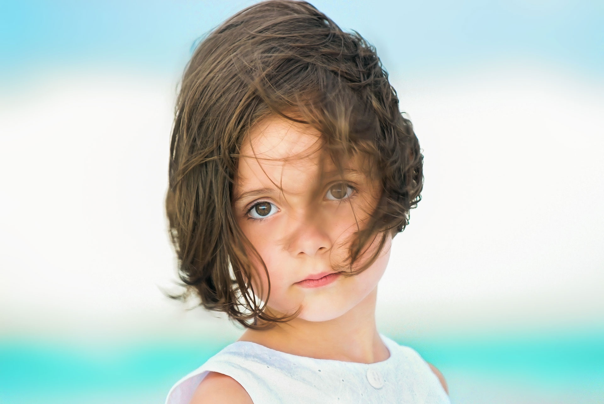 headshot of little girl with big brown eyes in white top with hair blowing in wind