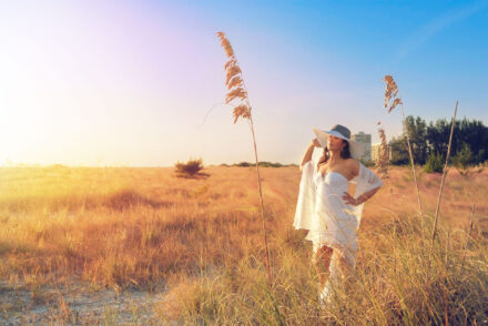 woman in white dress and wide brimmed hat standing in sea oat on Siesta Key beach