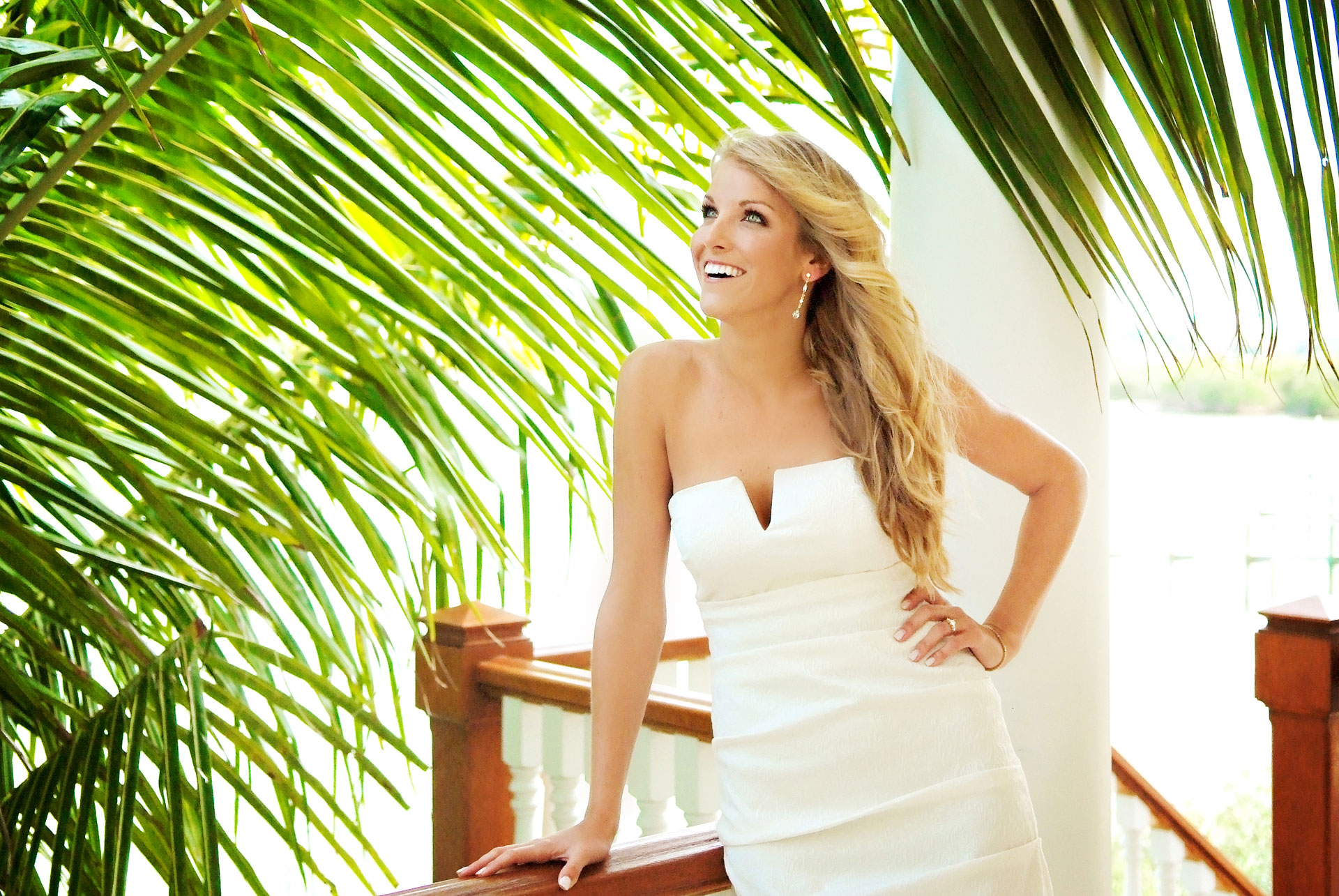 blond bride standing on balcony with hand on hip and large green palm tree leaves