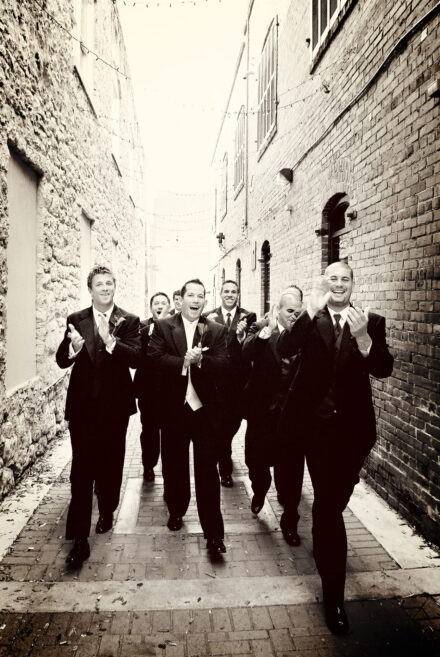 group of groomsmen clapping and walking in alley