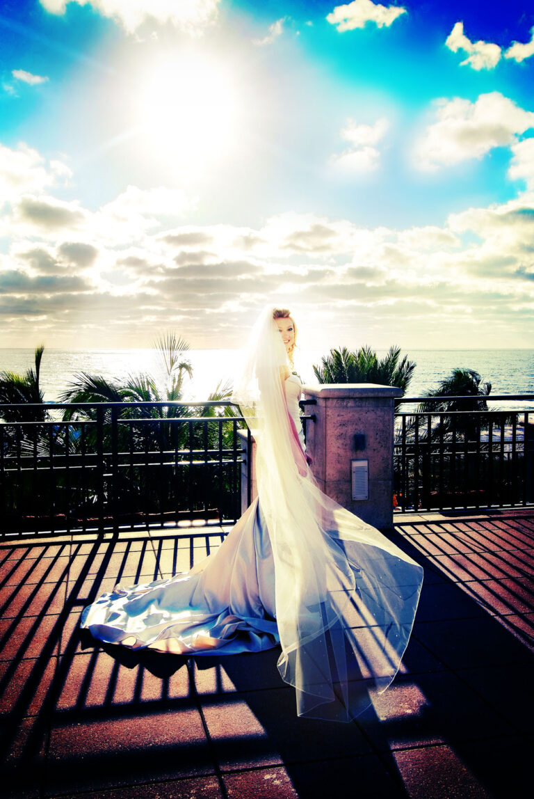 bride with flowing veil on balcony with beach and sky background