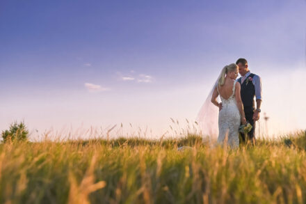 groom and back of bride's dress standing in seagrass and oats on anna maria island against blue sky