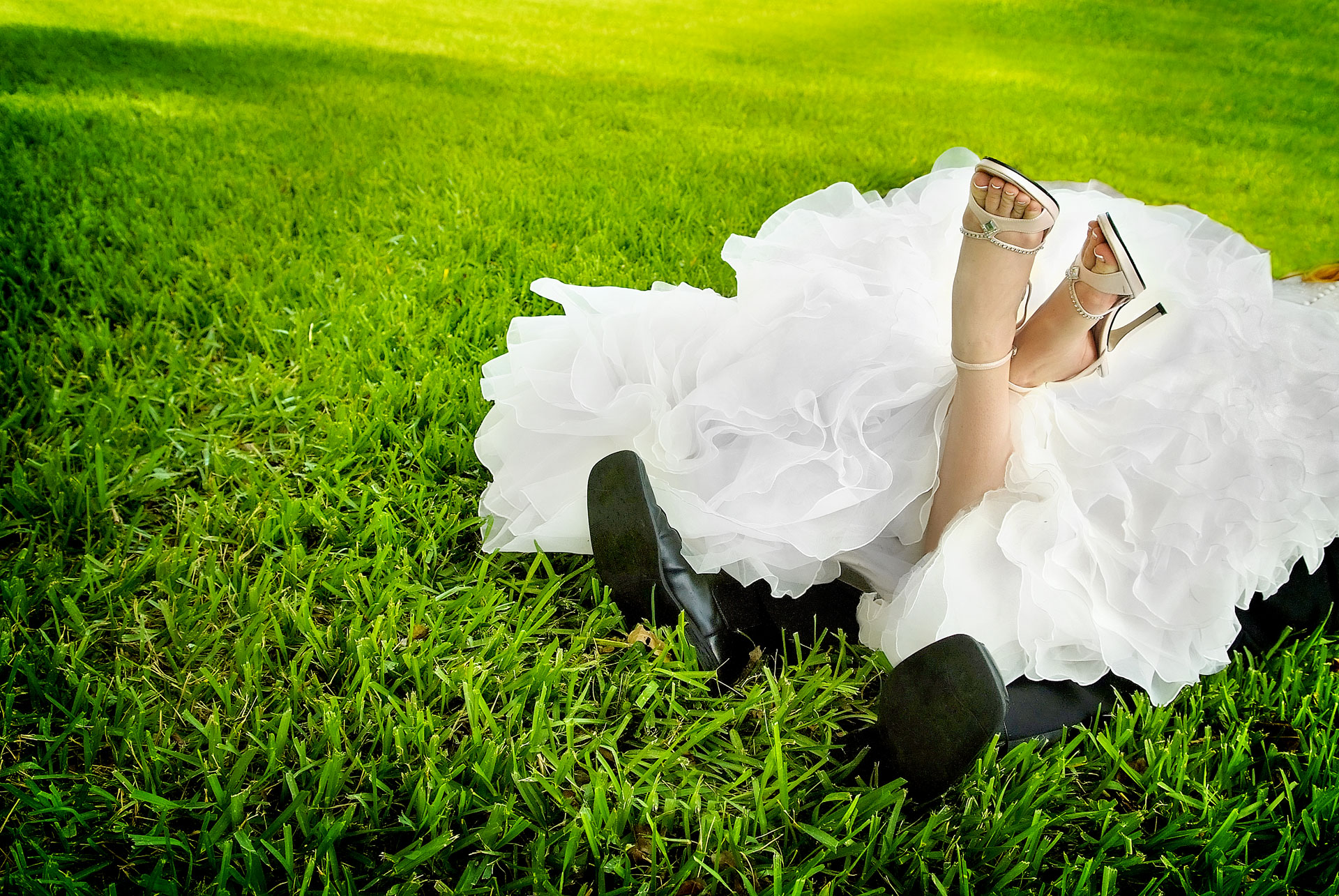 bride with white heels on lying on groom with black dress shoes on in grass at ringling museum lawn with only feet showing