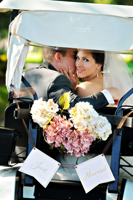 groom kissing bride on cheek while she looks back in back of golf card with just married sign and flowers