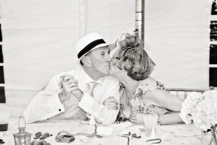 older British wedding reception guests with fun hats kissing with eyes open at table